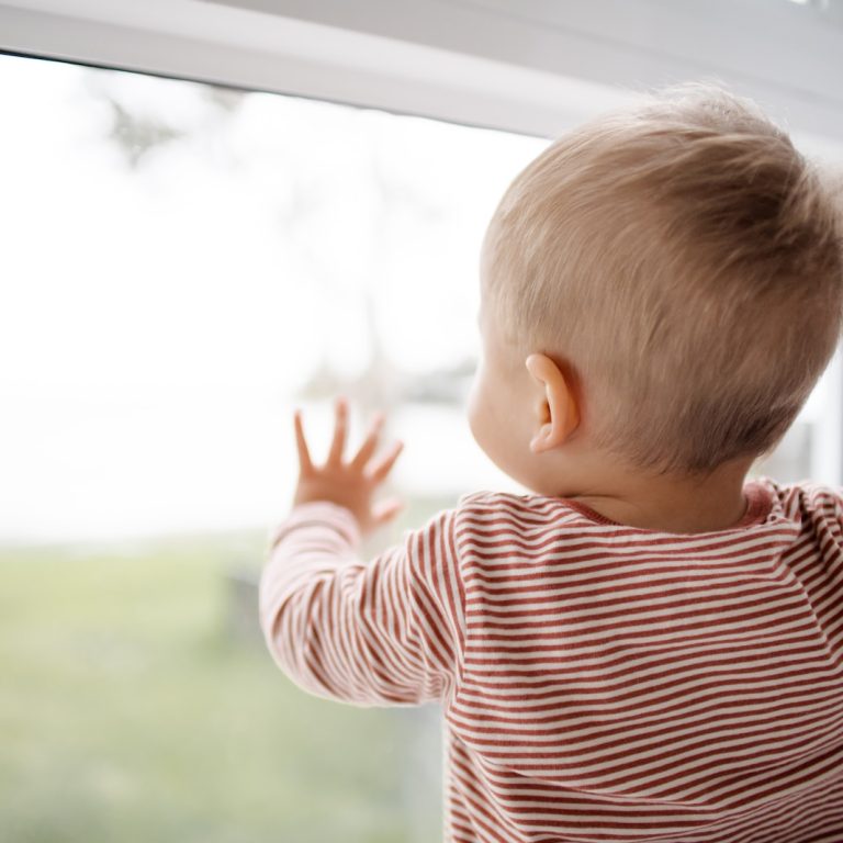 child in red and white striped shirt looking out the window